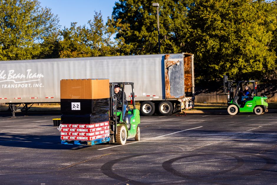 Forklift operators loading pallets onto a truck outdoors on a sunny day. Efficient warehouse logistics in action.